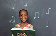 Girl holding a hymn book with music notes on a chalkboard behind her